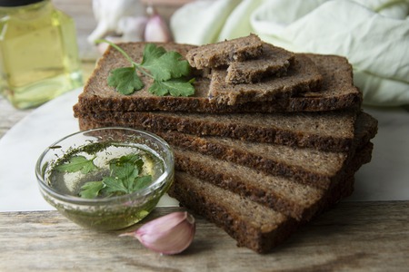 Sliced wholegrain bread wit seeds, greens, oil and garlic on cutting board. Top view.の写真素材