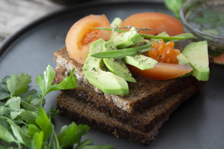 Healthy avocado sandwich on dark rye toast bread made with fresh sliced avocado, seeds and tomatoes on rustic background.の写真素材