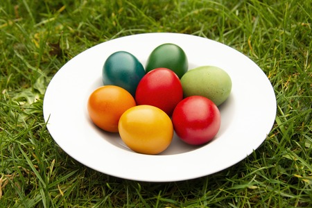Easter eggs pile in white plate. Colorful, red, green ,blue, yellow and orange eggs, garden view.の写真素材