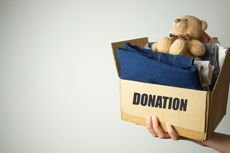 Donation concept. Kid holding donate box with clothes, books, school supplies and toysの写真素材