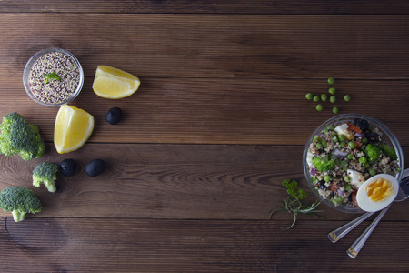 Bowl with quinoa and different vegetables - egg, broccoli, tomato, green peas, red onions. Wooden table.の写真素材