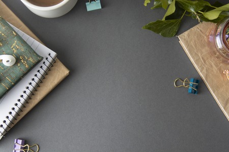 Desk table with blank notebook, office supplies, green plant and coffee cup. Grey Flat lay with copy...