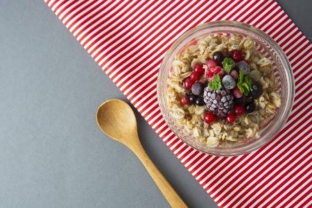 Healthy breakfast in a bowl with oatmeals, frozen berries, fresh strawberries, mint.の写真素材