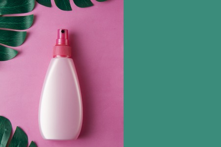 Summer abstract, pink background. Sunscreen bottle with monstera leaves, copy space.の写真素材