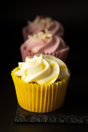 Pink and yellow cupcakes against a black background, birthday or party cupcakes. Party sweet food, desserts.の写真素材
