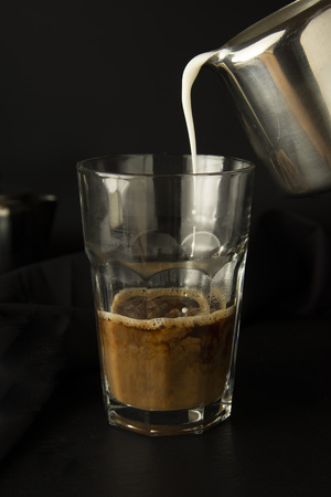 Pouring milk in glass of coffee. Cold, refreshing, caffeine milkshake. Summmer drink. Black backgroundの写真素材