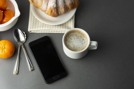 Delicious breakfast coffee with croissant. Heart shaped box. Work table with smart phone. French pastry and cup of coffee. Template for social media. New day.の写真素材