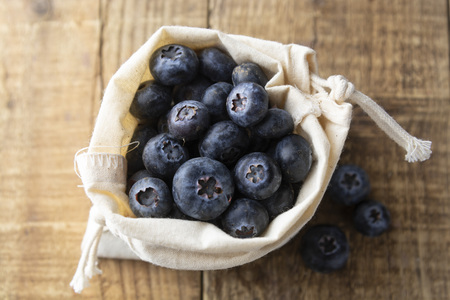 Blueberries spilling out of a brown textile, eco bag over rustic wood table. Zero waist concept, no plastic. Eco friendly berries, fruits.の写真素材