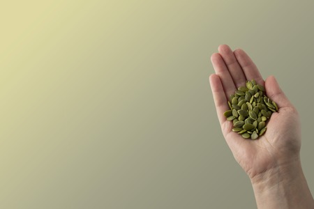 Woman holding raw unshealead pumpkin seeds, closeup view, isolated. Healthy, vegetarian super food or snack. Template for design.の写真素材