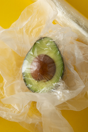 Close up green Avocado in plastic bag for sale or fridge. Effect Destroyer of the use of plastic bags. Zero waste concept. Avocado isolated on yellow background. No palstic background.の写真素材