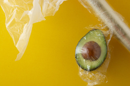 Close up green Avocado in plastic bag for sale or fridge. Effect Destroyer of the use of plastic bags. Zero waste concept. Avocado isolated on yellow background. No palstic background.の写真素材