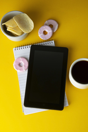 Styled yellow, food backdrop. Unhealthy lunch, snack with coffee, cookies, digital tablet. work space, lunch at work table. Top view. Copy spaceの写真素材