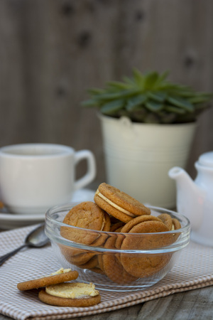 Ginger cookies with cream, biscuit for tea of coffee, on wooden table. Sweet healthy food snack with tea cupの写真素材