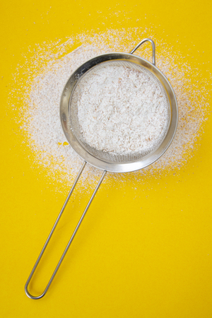 Sieve with flour heaped on yellow background. Creative food concept, baking, recipes, pastry.の写真素材