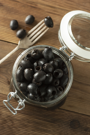 Black olives or pickled olives in jar on wooden background.の写真素材