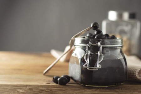 Black olives isolated, mason jar, wooden background. Mediteranian foods. Copy spaceの写真素材
