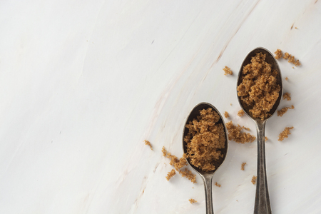 Brown sugar in metal spoons on bright, marble background with copy space. Dessert ingredient, sugar addictedの写真素材
