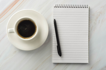 Open notebook with cup of coffee on marble desk. Workplace, work table.の写真素材