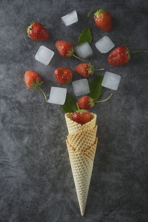 Strawberry fruits and mint leaves in waffle cone, over dark background, top view.の写真素材