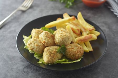 Chicken nuggets with french fries on dark background, top view, fast food.