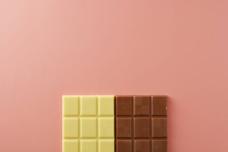 White and black chocolate bars over pink background, copy space, top view.の写真素材