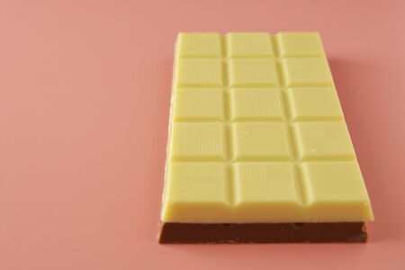 White and black chocolate bars over pink background, copy space, top view.