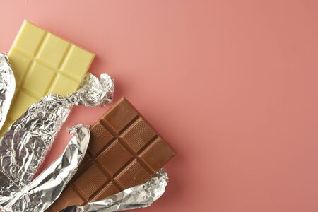 White and black chocolate bars over pink background, copy space, top view.