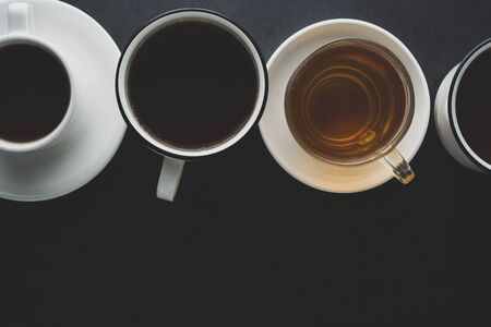 Top view of many cups, mugs with hot tea drink on dark background, copy space. Tea time or tea brake. Autumn toned, dark photo.の写真素材
