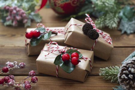 Close up Christmas gift boxes wraped in craft paper, fir branches, red baubles, pine cones over...