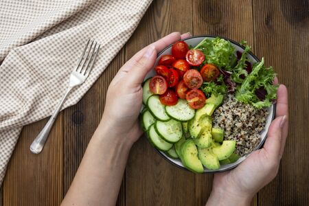 Woman hand holding  bowl with quinoa, avocado, cucumber, salad, tomatoes, olive oil.の写真素材