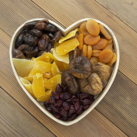 Dried fruits mix, in wooden heart shape box isolated on woodenの写真素材