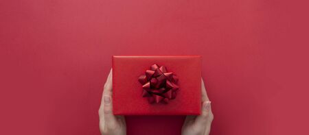 Top view of female hands holding gift box with red ribbon bow isolated over flat lay background,...