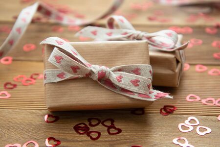 Kraft brown paper gift box with red bows and confetti on wooden
