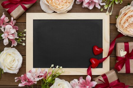 Gift boxes with red ribbon, flower arrangement and empty chalkboard on wooden table.の写真素材