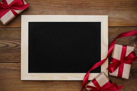 Gift boxes with red ribbon and empty chalkboard on wooden table.の写真素材