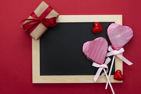 Valentine's Day mock up, chalkboard with lollipop in the shape of a heart, gift boxes and glitter isolated on red background, copy space for text.の写真素材