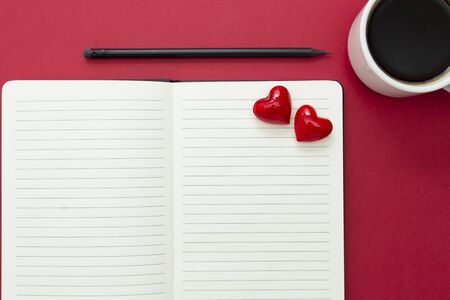 Valentine's Day. Open notebook with red hearts and a pencil, on red background, copy space.の写真素材
