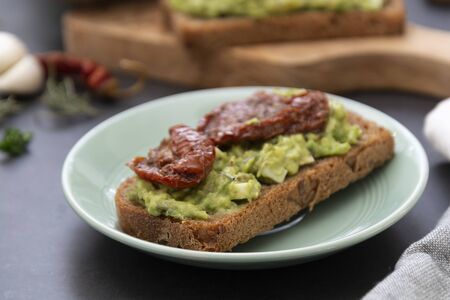 Healthy food. Rye bread with guakomole, avocado pasta and dried tomatoes, on wooden cutting board. Avocado toast, isolated.の写真素材