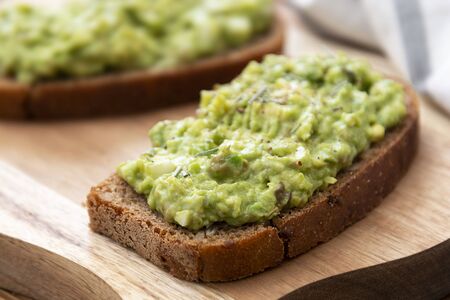 Healthy food. Rye bread with guakomole, avocado pasta on wooden cutting board. Avocado toast for...