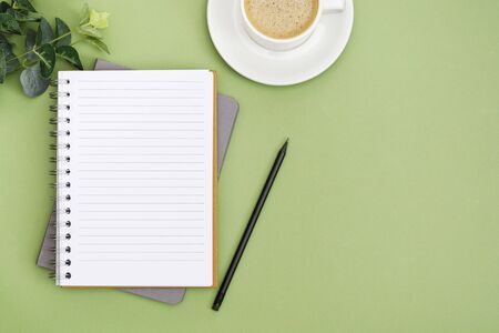 Open notebook with empty page and coffee cup. Table top, work space on green background. Abstract...