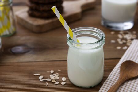 Glass jar, bottle of oat milk with paper straw on wooden background with copy space for text.の写真素材