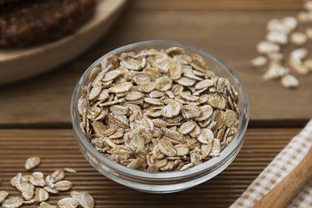 Raw oat-flakes in glass bowl on wooden spoon on wooden table. Healthy breakfast.