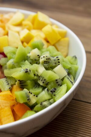 Fresh fruits salad - mango, citrus, kiwi fruit, plum and persimmon. Wooden background, flat lay, top view healthy food.の写真素材
