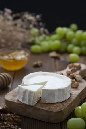 Goat cheeses on wooden background with honey and grapes. Dark food photography.の写真素材