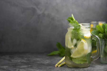Glass mason jar of ice tea with fresh mint, lemon and paper straw on dark background. Summer healthy cold drink.の写真素材