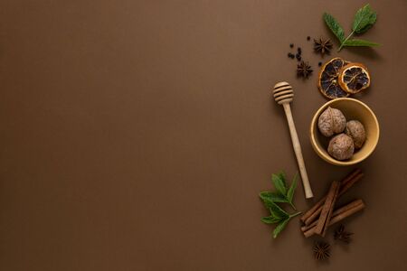 Condiments and spices, honey spoon, anise star, cinnamon sticks, mint leaves, brown background top...