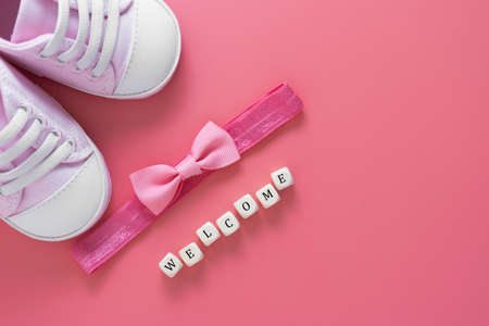 Baby girl pink background with newborn shoes, bow and Welcome words. Baby flat lay.の写真素材