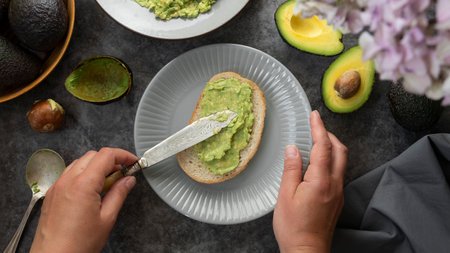 Avocado toast. Womans hands spreading avocado pasta on bread slice. Healthy food concept.