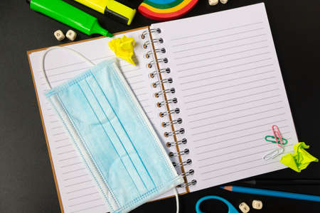 Top view of open notebook with face mask, colorful pencils, rainbow eraser, notebook, sticky notes. Flat lay.の写真素材