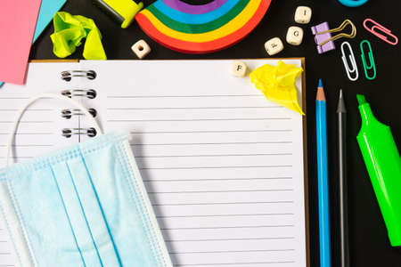 Top view of open notebook with face mask, colorful pencils, rainbow eraser, notebook, sticky notes. Flat lay.の写真素材